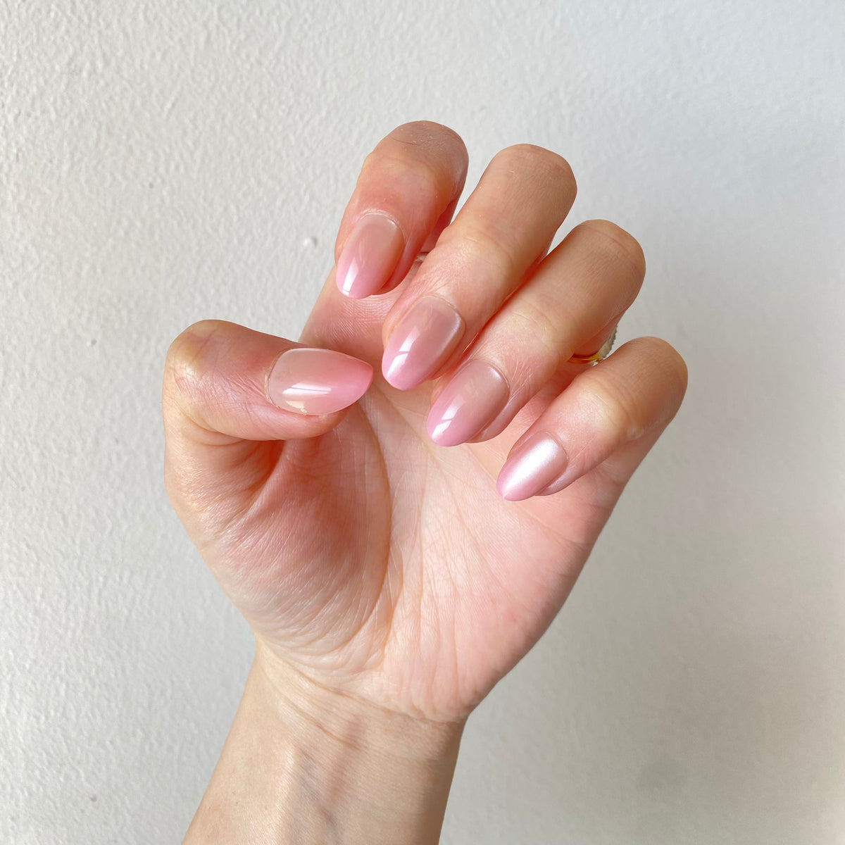 Pearl blush chrome press-on nails fist pose against white wall