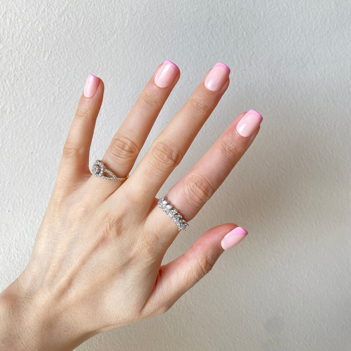 Baby pink glazed press-on nails spread hand against linen with rings