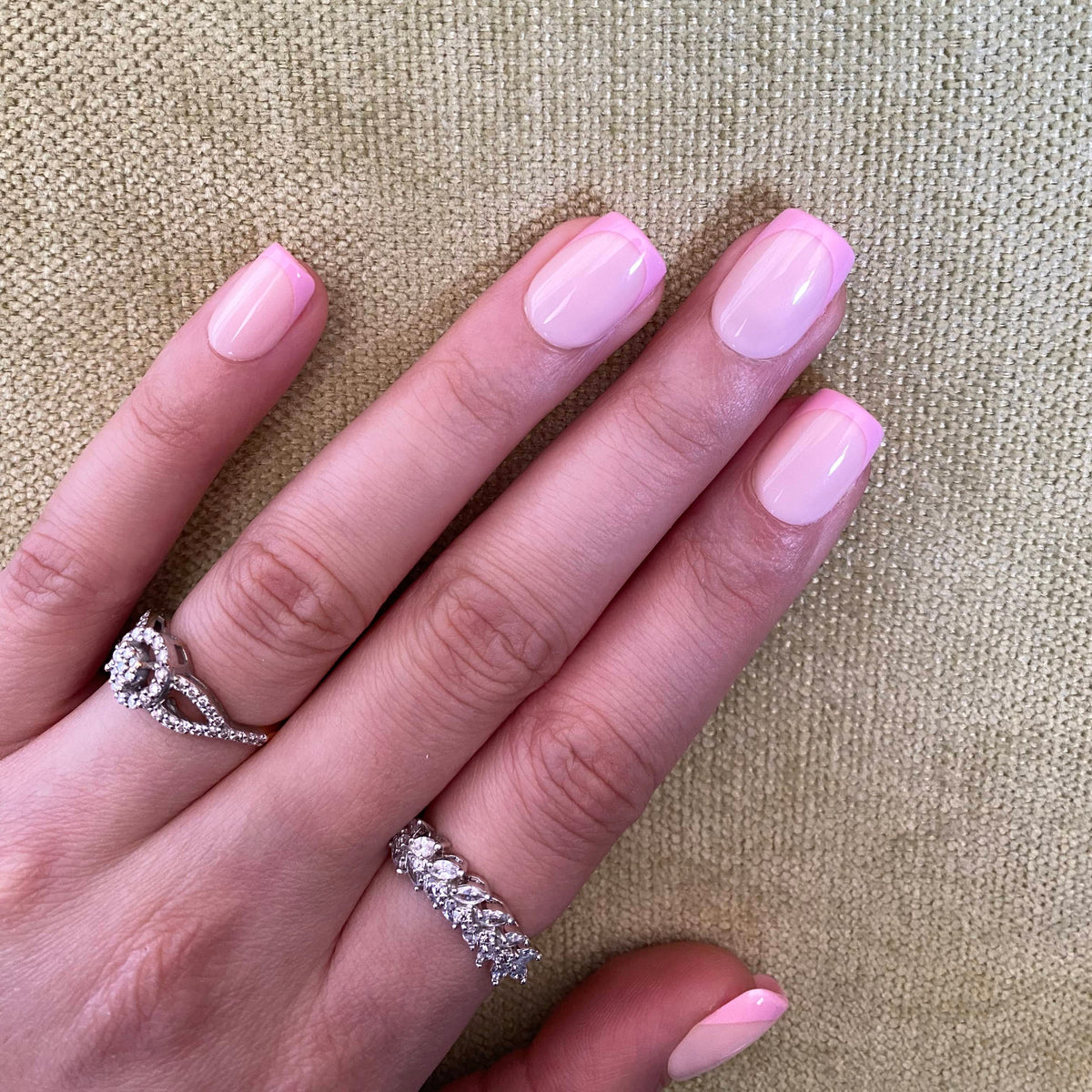 Baby pink glazed press-on nails curled fist pose against linen