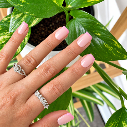 Baby pink glazed press-on nails with silver rings against greenery