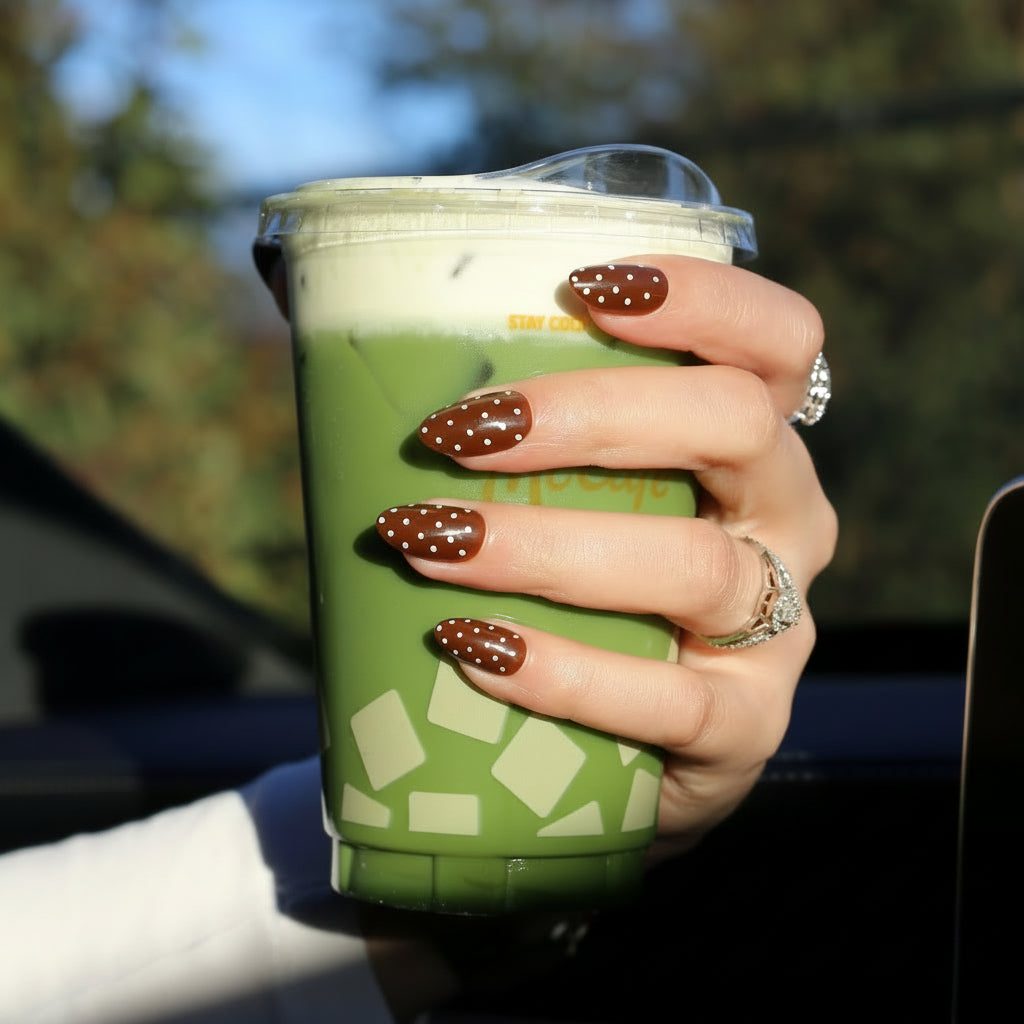 Hand holding an iced matcha drink showing brown polka dot almond press-on nails